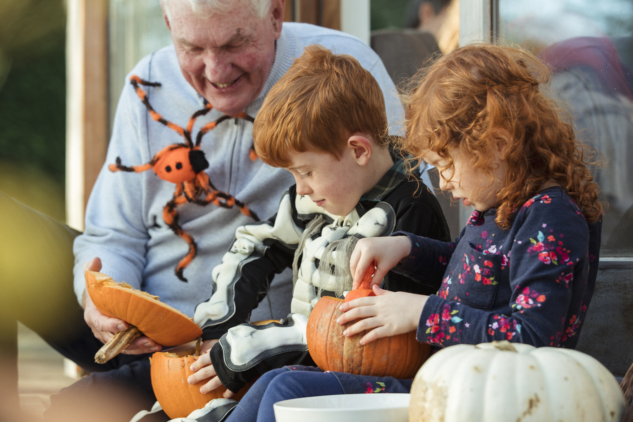 Two children and their grandfather are decorating pumpkins together on the porch step.