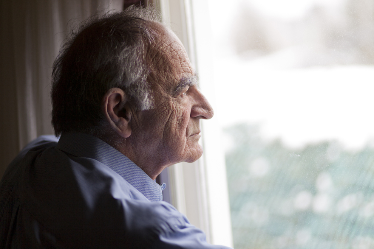 Senior man looking out of widow on dreary day