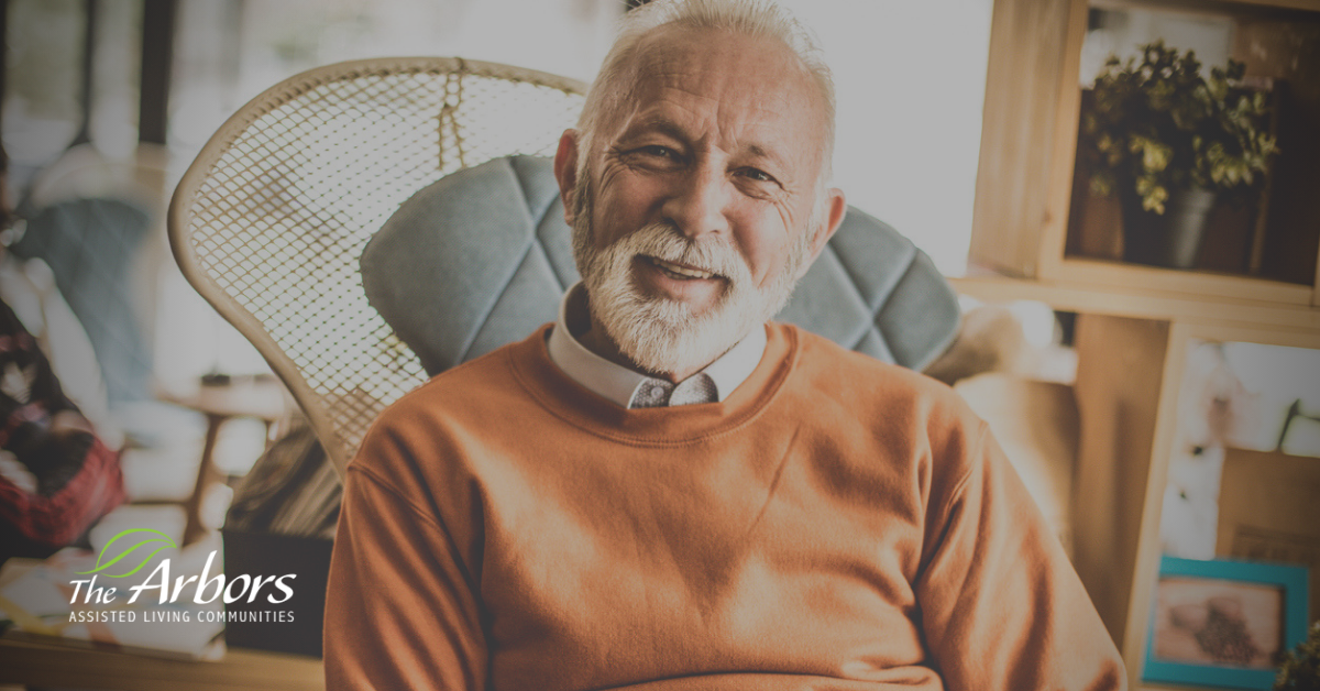 elderly man with short white beard sitting on chair happy and smiling.