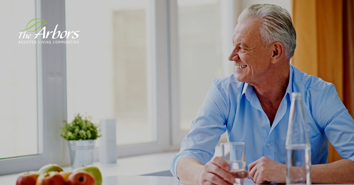 elerly man smiling drinking water at kitchen table