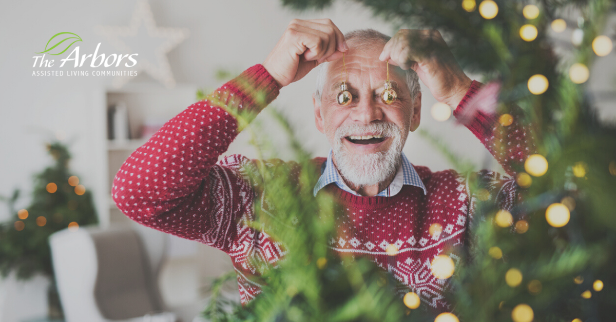 Elderly man with white beard smiling with christmas ornaments over his eyes being silly.